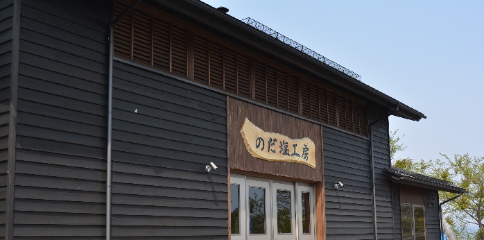 のだ塩工房の看板が掲げられている黒い外壁の建物の外観写真