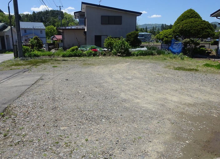 奥に2階建ての住宅がある、地面が砂利の広々とした北区地区の空き地の写真