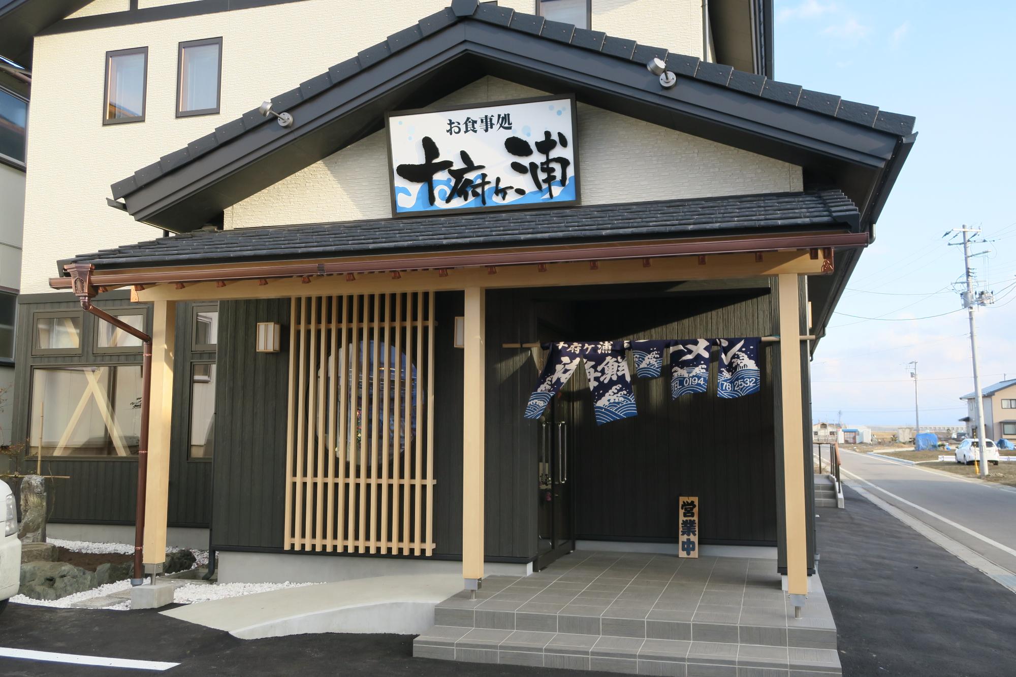 玄関上の壁に「十府ヶ浦食堂」の看板があり、瓦屋根で黒とクリーム色を基調とした外壁の十府ヶ浦食堂の外観写真