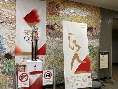 役場村民ホールに展示された聖火リレートーチと横断幕の写真