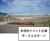 多目的イベント広場サークルステージ：手前にピンクや赤色の花が植えられた花壇があり、奥に円形をしたサークルステージが見えている写真