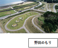 野田のもり：左上に海が少し見え、手前に芝生で整備された広場が広がっている野田のもりを少し高い場所から写した写真