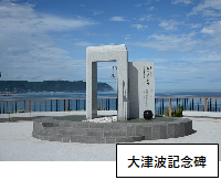 大津波記念碑：奥に海が見えており、鐘が付いているコンクリートで出来た記念碑を中心に写した写真