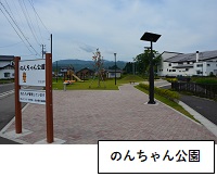 のんちゃん公園：左側に「のんちゃん公園」と書かれた看板が立ち、奥の芝生が広がる場所に遊具が設置してある写真