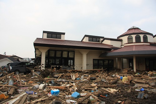 1台の車が建物に突っ込み、瓦礫が建物周辺一帯に広がっている野田村生涯学習センター被害状況の写真
