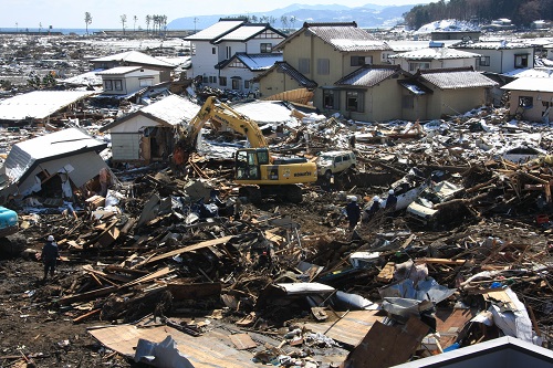 沢山の瓦礫が押し寄せた住宅街で1台のショベルカーが作業をしている写真