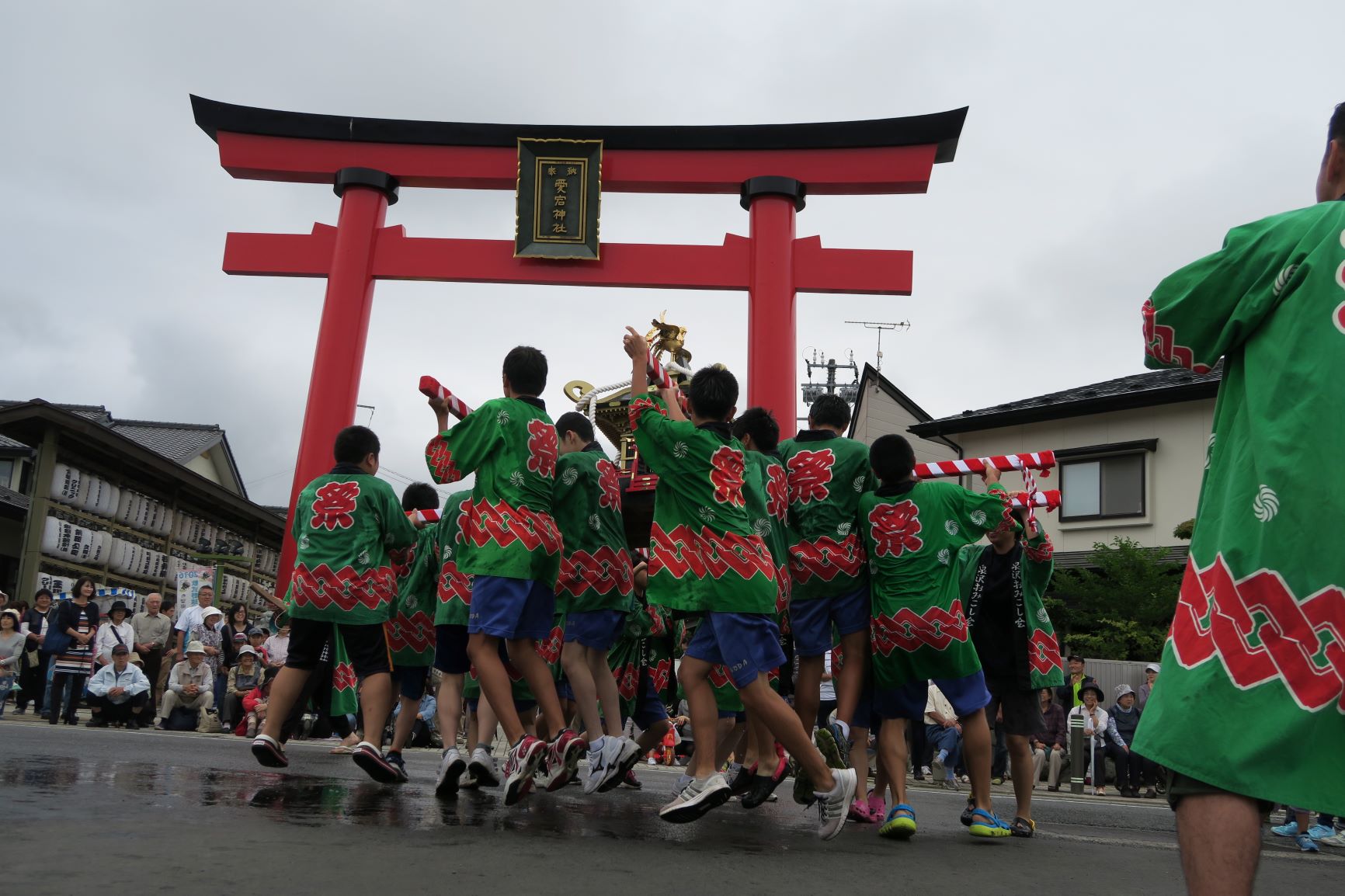 緑の法被を着た人たちが、赤い鳥居の前で神輿を担いでいる写真