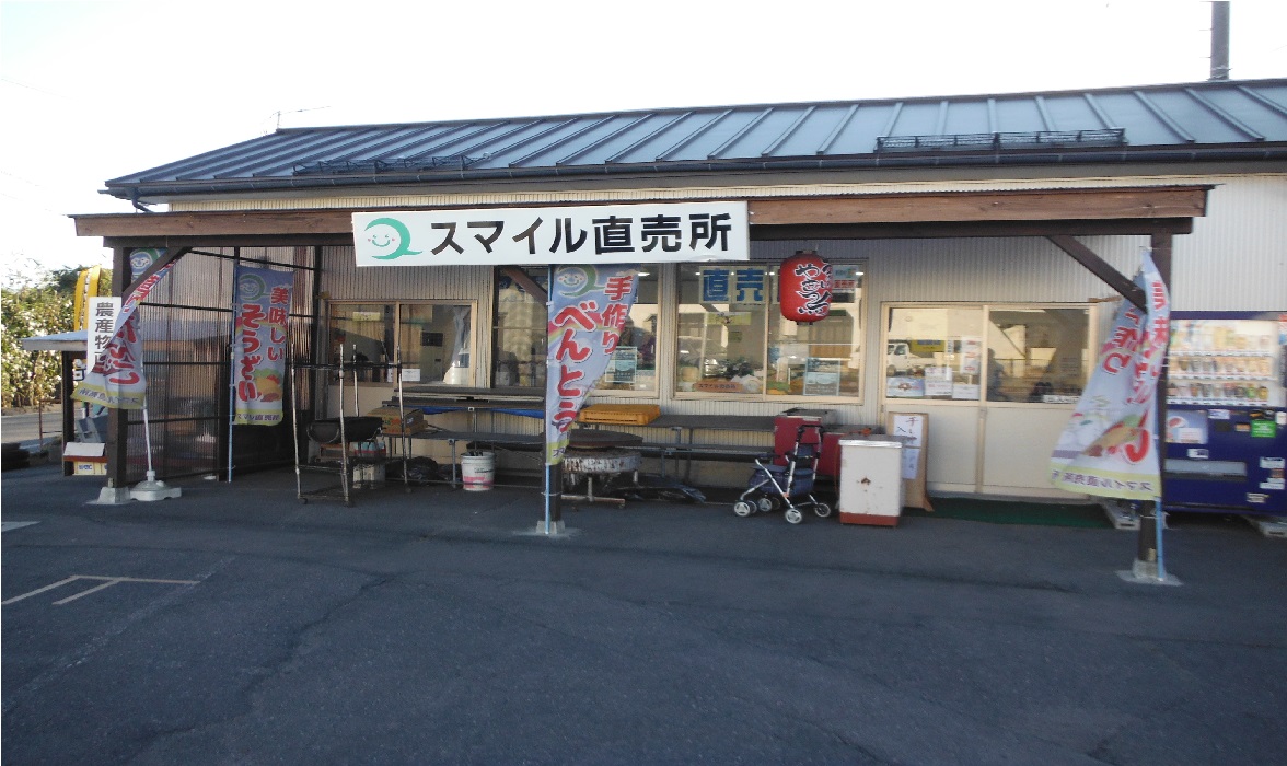 「スマイル直売所」の看板と「手造りお弁当」と書かれたのぼり旗が店舗前にあるスマイル直売所の外観写真