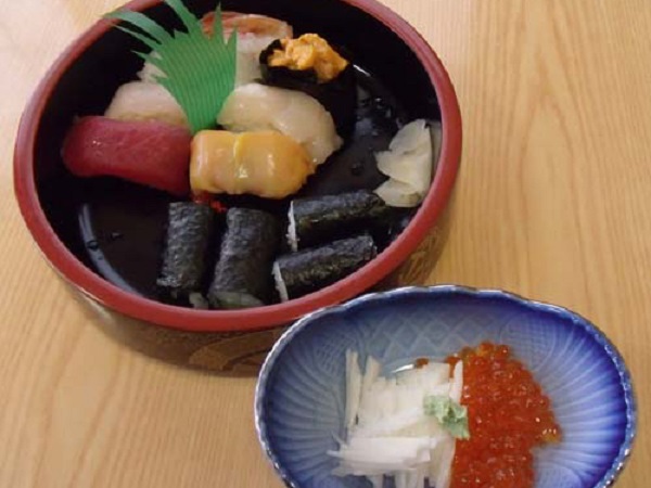 丸桶に盛り付けられたマグロや貝などの握り寿司と小皿に添えられた長芋の短冊切りといくらの写真