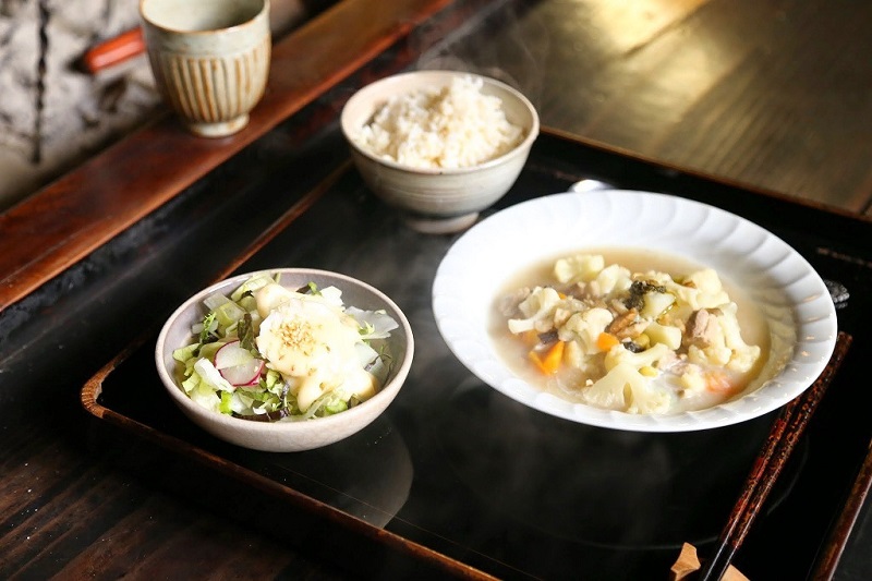 ご飯、サラダ、野菜の沢山入ったシチューがお盆に並べられている日替わりランチの写真