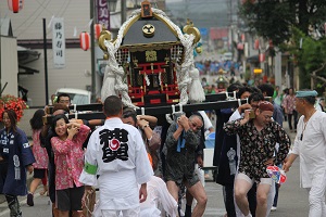担ぎでの男性と女性が神輿を担いでいる沿道を運行している祭りの様子の写真