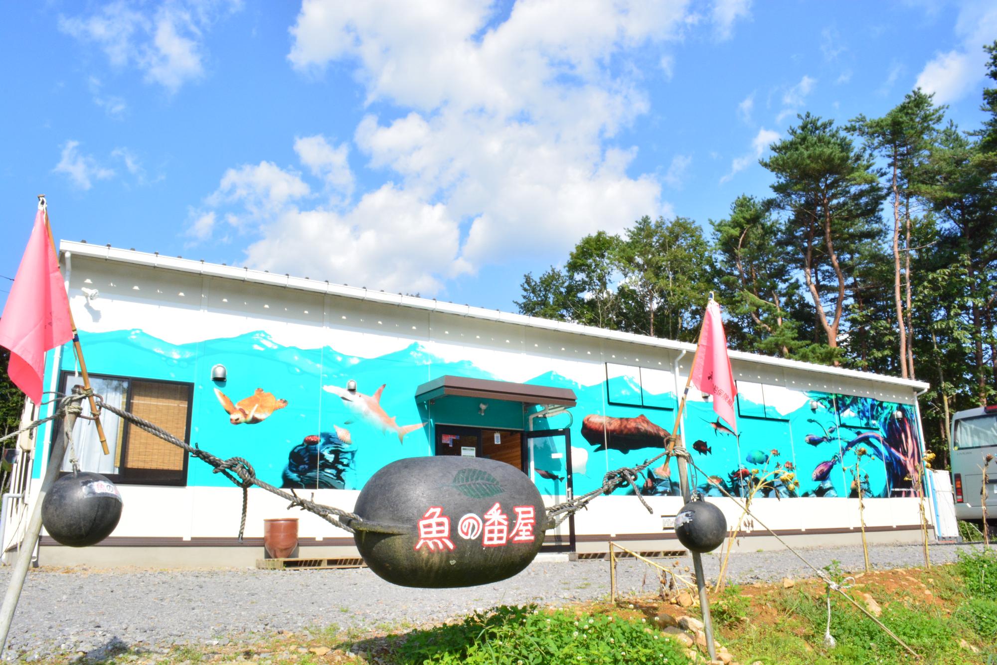 魚の番屋と書かれたブイの奥に見える美術館の建物の写真