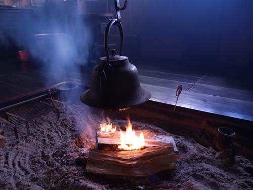 囲炉裏の中心に炎があがっており、その上に鉄瓶が吊るされている写真