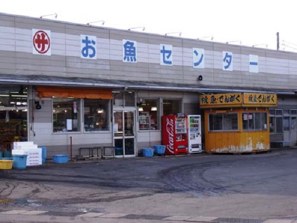 店舗入り口の上部に「お魚センター」と表示があり、入り口横には「焼き魚・でんがく」の出店があるお魚センターの外観写真