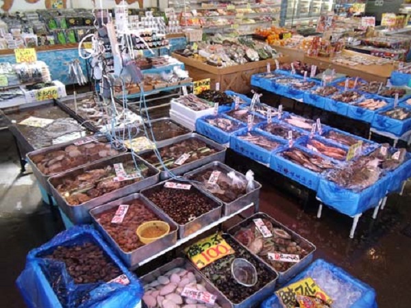 沢山の新鮮な魚介類が種類ごとに分けて並べられ、奥には野菜なども並んでいるお魚センターの店内の写真