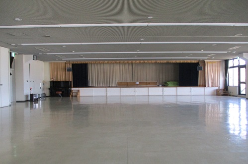 前方に幕がついた舞台が設置されており、白い床で広々としたスペースの大会議室の写真