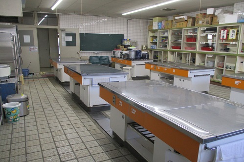 調理台が6つあり棚に調理道具や食器が置かれている調理講習室の写真