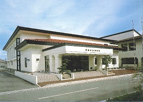 通り沿いに面している、玄関前に数段の階段がる白い外壁の野田村体育館の外観写真