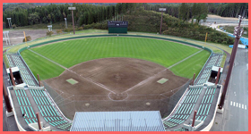 階段状の観客席があり、フィールドは、土の部分と芝の部分があるライジング・サン・スタジアムを上空から写した写真