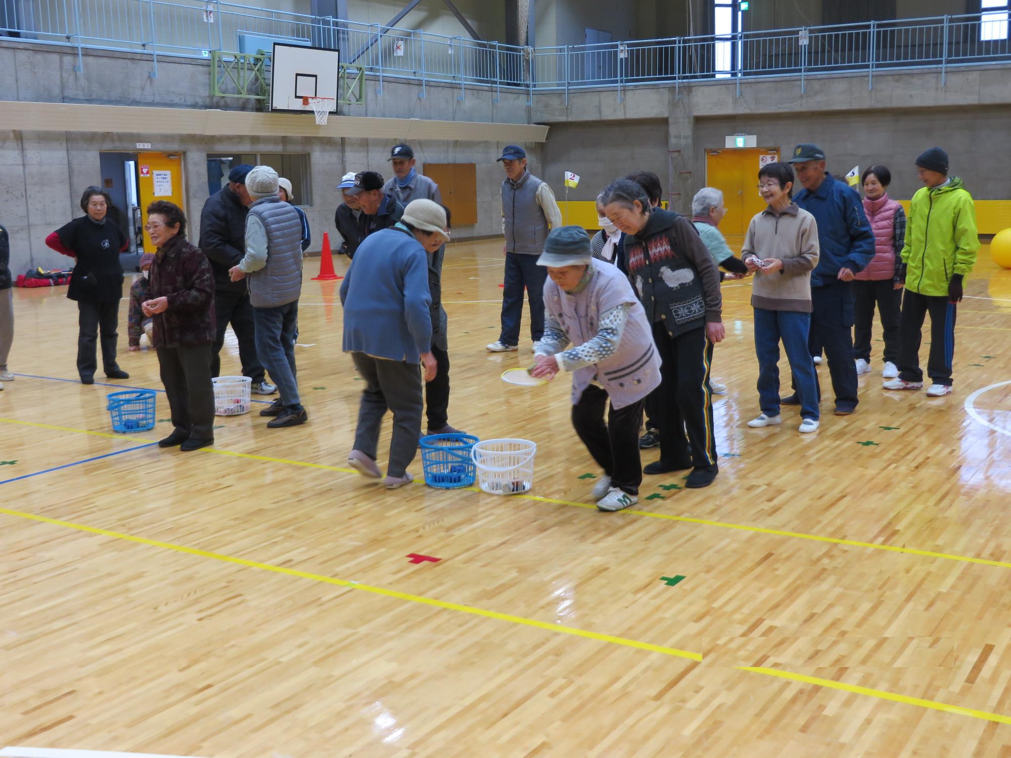 2組に分かれた人達が体育館の床に置かれた白と青のかごの中にお手玉のようなものを順番に入れるスポーツをしている写真