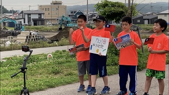 オレンジ色のシャツを着た4名の男の子が横一列に並んで応援メッセージの動画を撮影している様子の写真