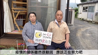 応援メッセージを書いた画用紙を手に持っている男性と女性が自宅の前に座っている動画の写真