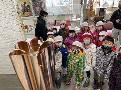 展示されている聖火リレートーチを、赤白帽を被った児童たちが眺めている写真