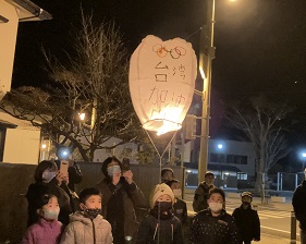 「台湾加油」と書かれた大きなランタンが浮かんでいる下で子供たちが並んで立っている写真