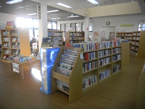 沢山の本が並んでいる本棚が室内に設置され、左側の窓から陽射しが入っている明るい雰囲気の図書館の写真