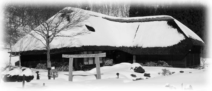 藁葺き屋根に雪が降り積もった古い平屋の建物の白黒写真