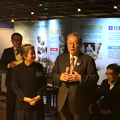 展示パネルの前に立ってマイクを持って話をしている小田村長の写真
