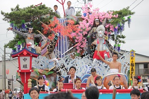 花や馬、波などで飾られた風流山車に太鼓を叩く子ども達が座り、演奏している祭りの様子の写真